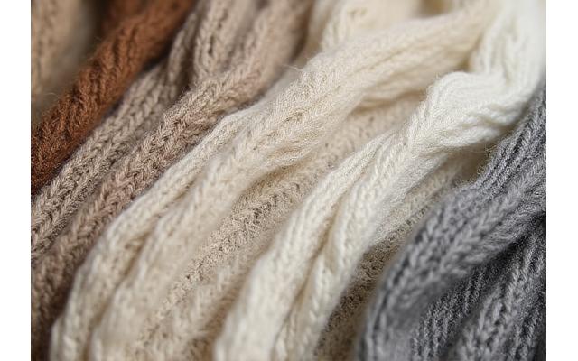Nærbilde av ulike naturlige tekstiler som ull, lin og bomull, i jordfarger.